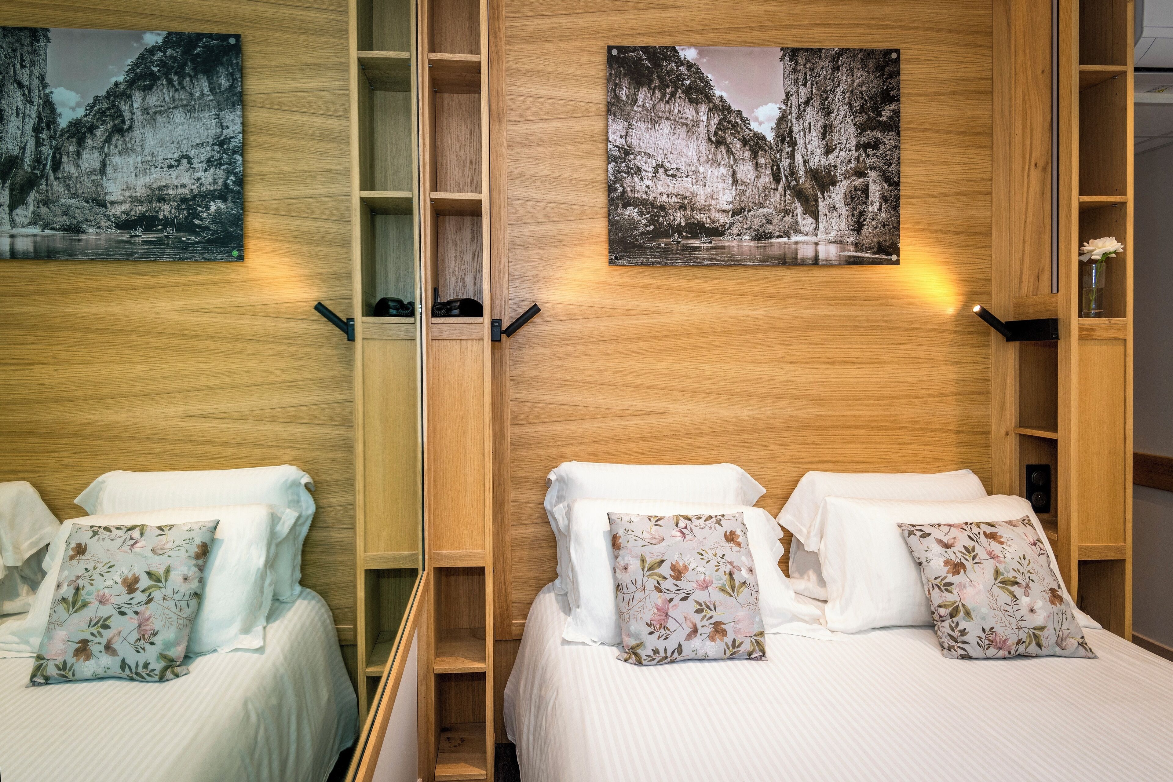 A hotel room with two beds, wooden headboards, and wall-mounted artwork.