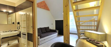 Et moderne værelse med en indbygget vask, en sovesofa, en lænestol og en stige til et loftrum.