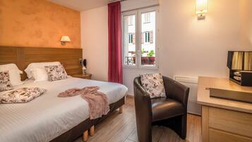 A hotel room with a bed, a desk, a chair, a window with curtains, and a lamp.