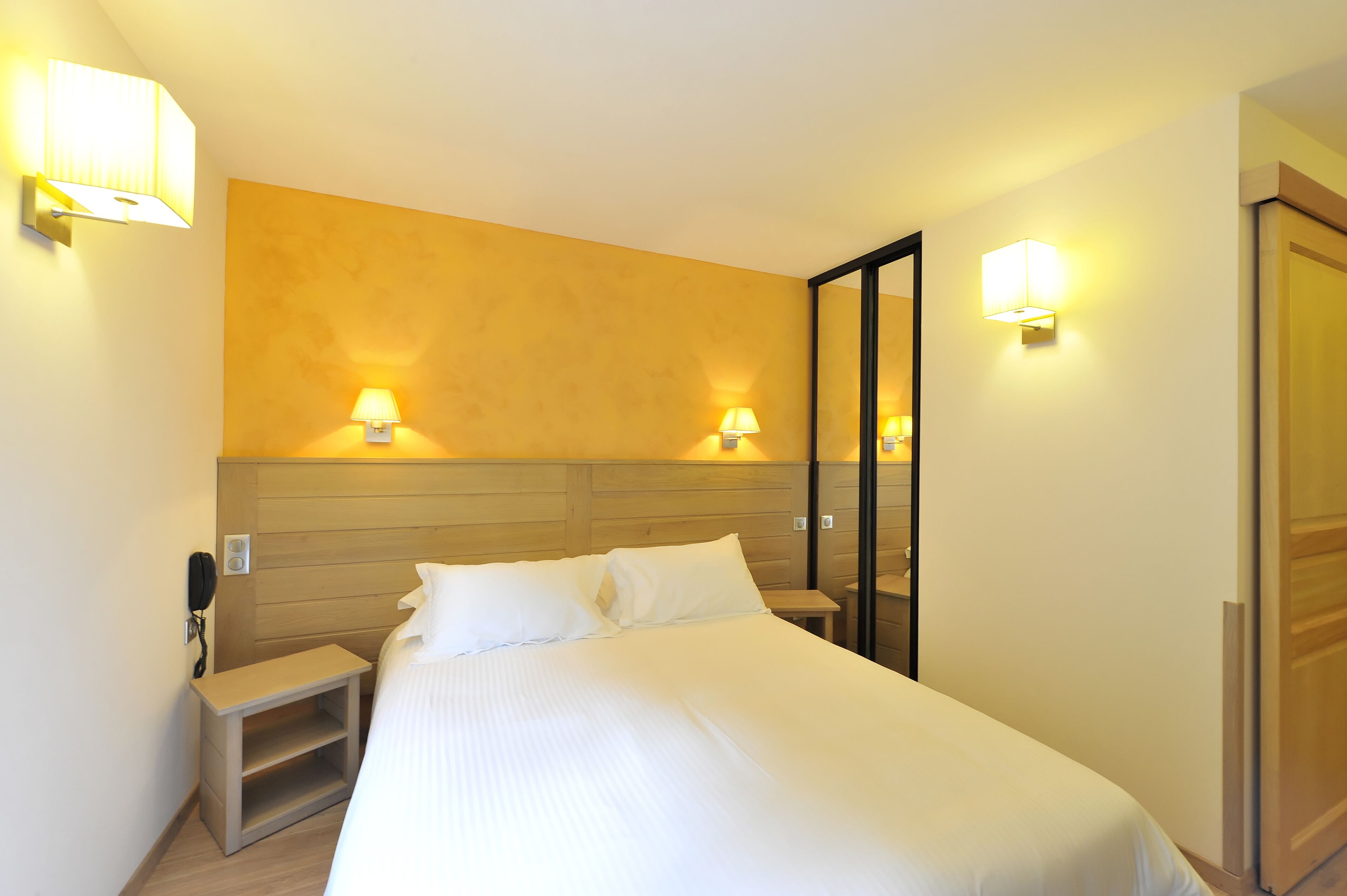 A hotel room with a large bed, bedside lamps, a wooden headboard, and a mirror.