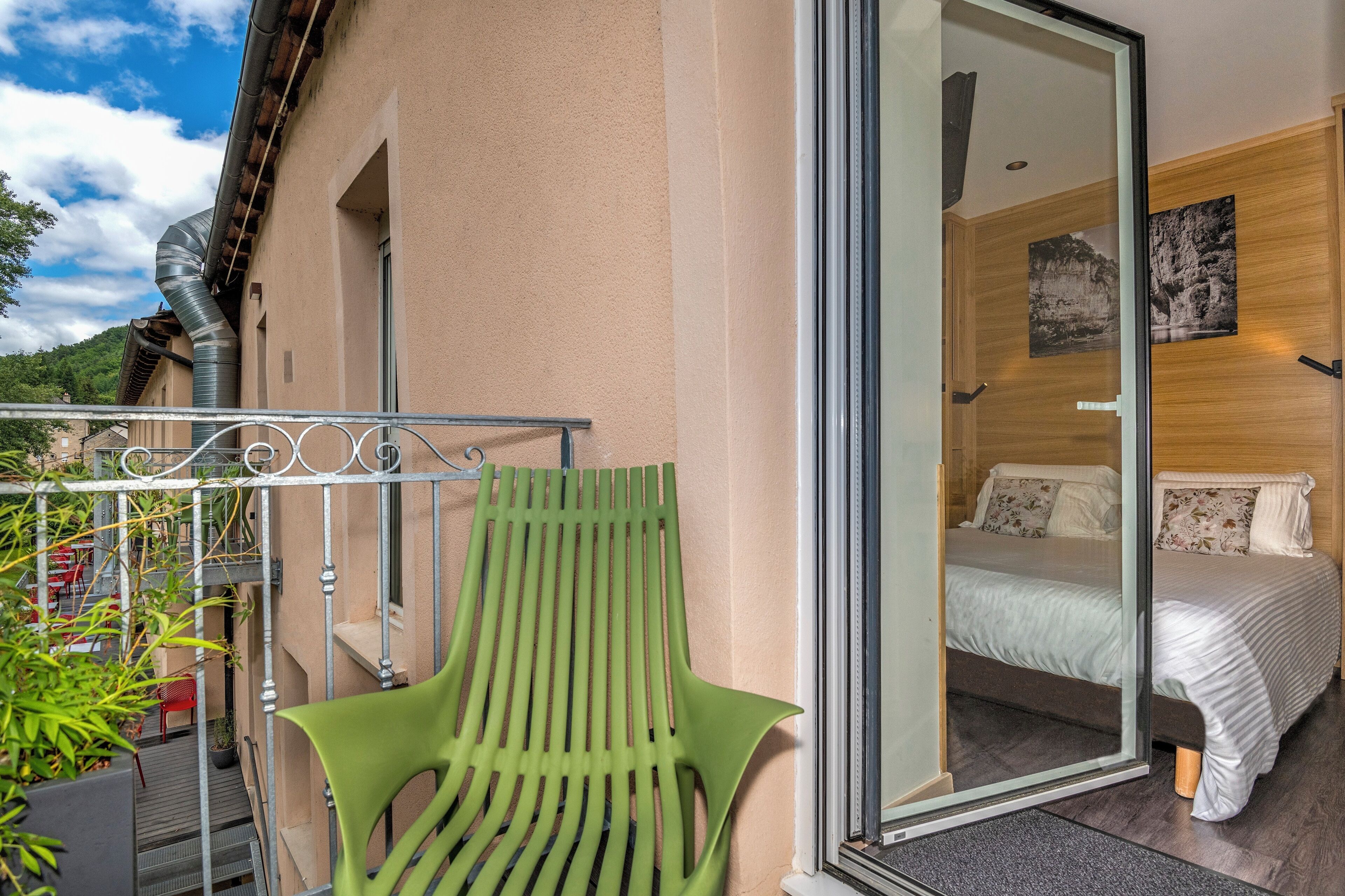 Un balcón con una silla verde, una cama con ropa blanca y una pared de madera con un cuadro.