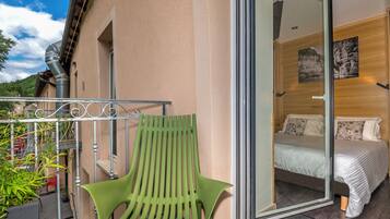 Un balcón con una silla verde, una cama con ropa blanca y una pared de madera con un cuadro.