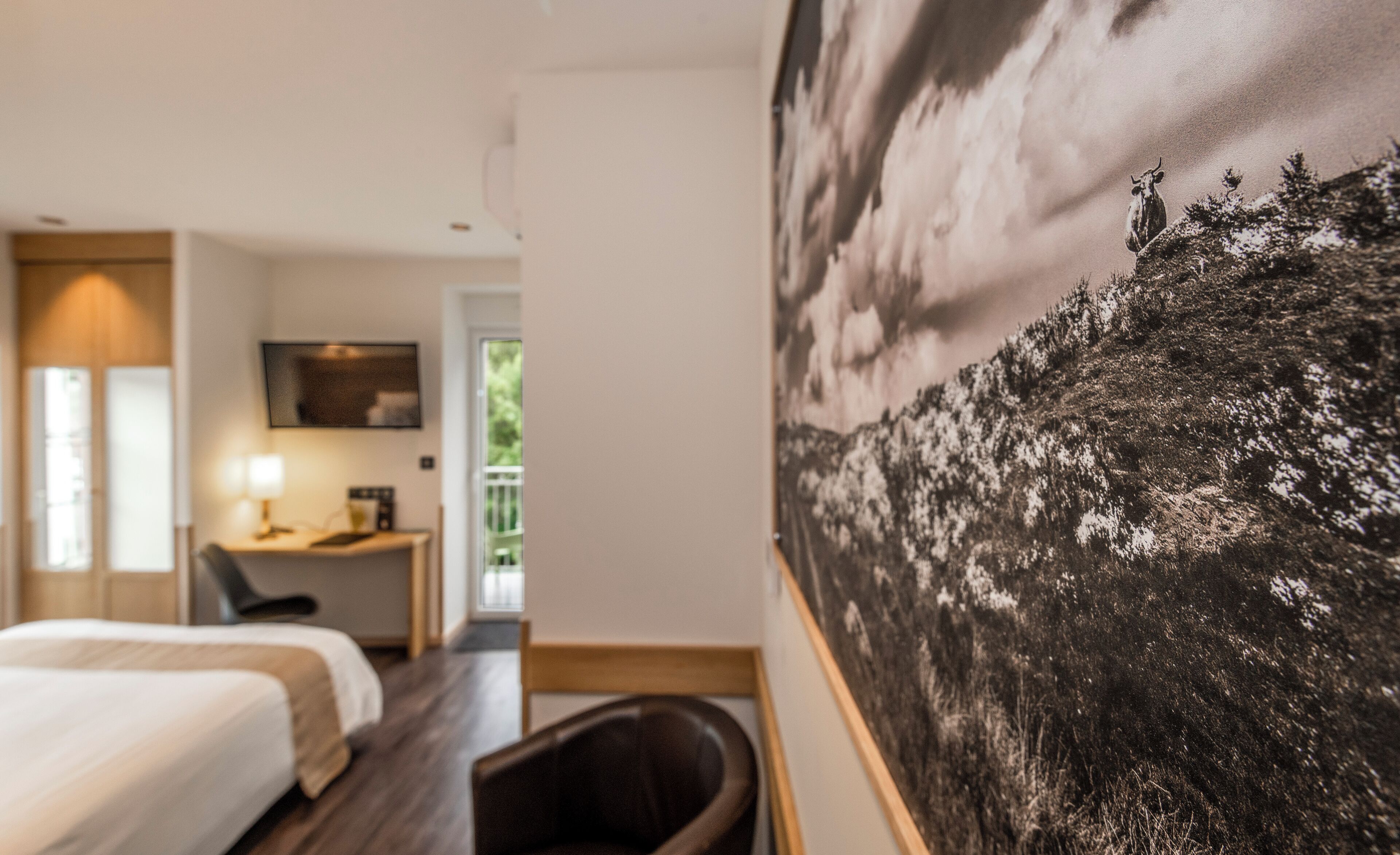 A hotel room with a bed, a desk, a chair, and a large painting on the wall.