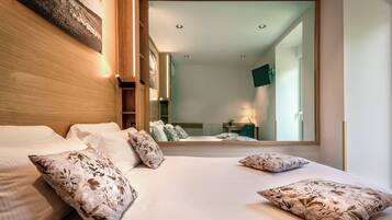 Una habitación de hotel moderna con una cama grande, almohadas estampadas con motivos florales, un cabecero de madera, un espejo amplio y vistas de la habitación contigua.