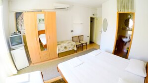 Habitación de hotel con dos camas, un escritorio, un armario y un baño visible a través de una puerta abierta.