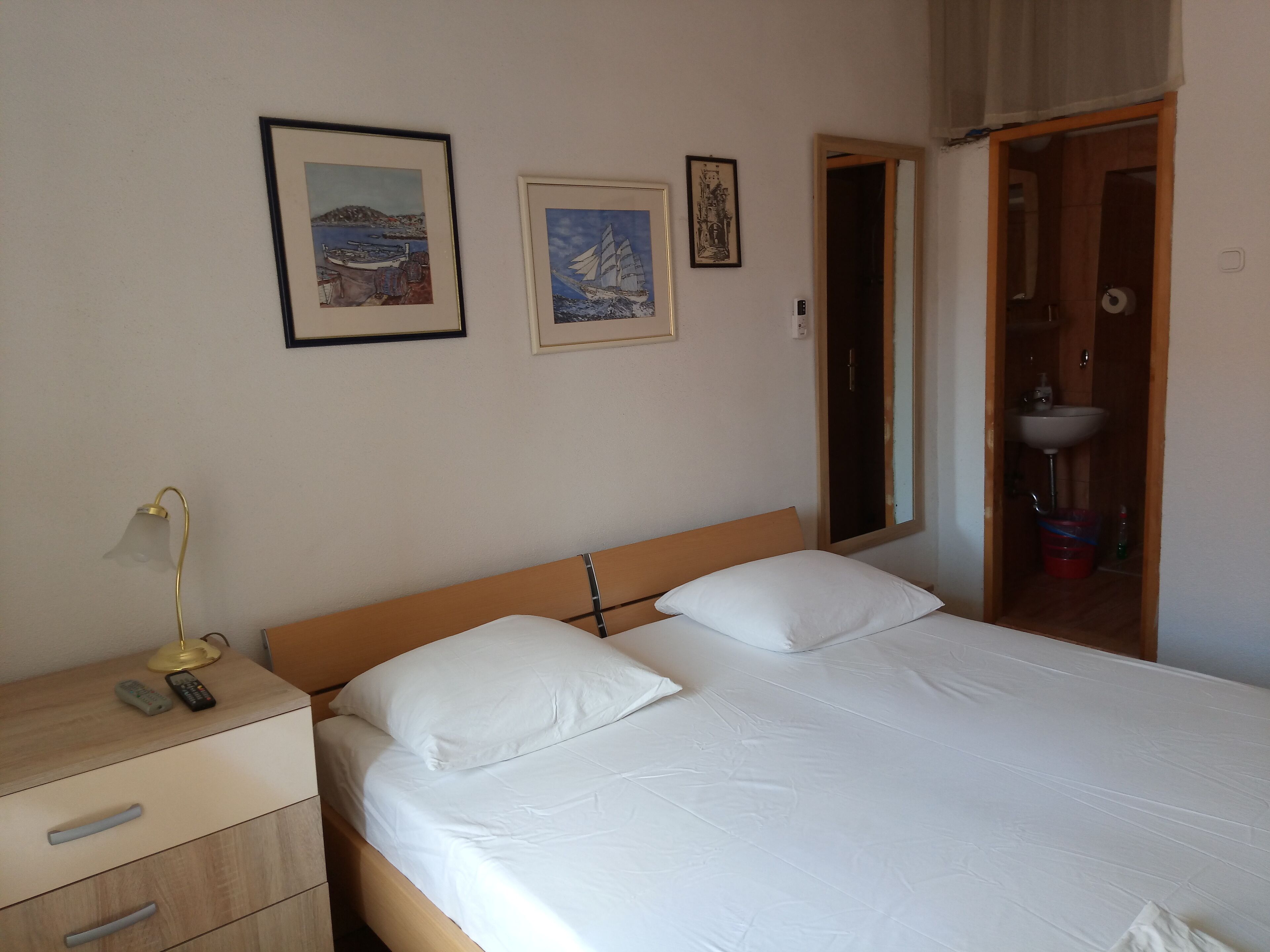 A bedroom with a bed, a bedside table with a lamp, and two framed pictures on the wall.