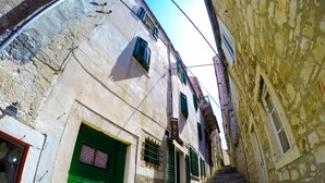 Una estrecha escalera de piedra que sube a un edificio con una puerta verde y varias ventanas con contraventanas.
