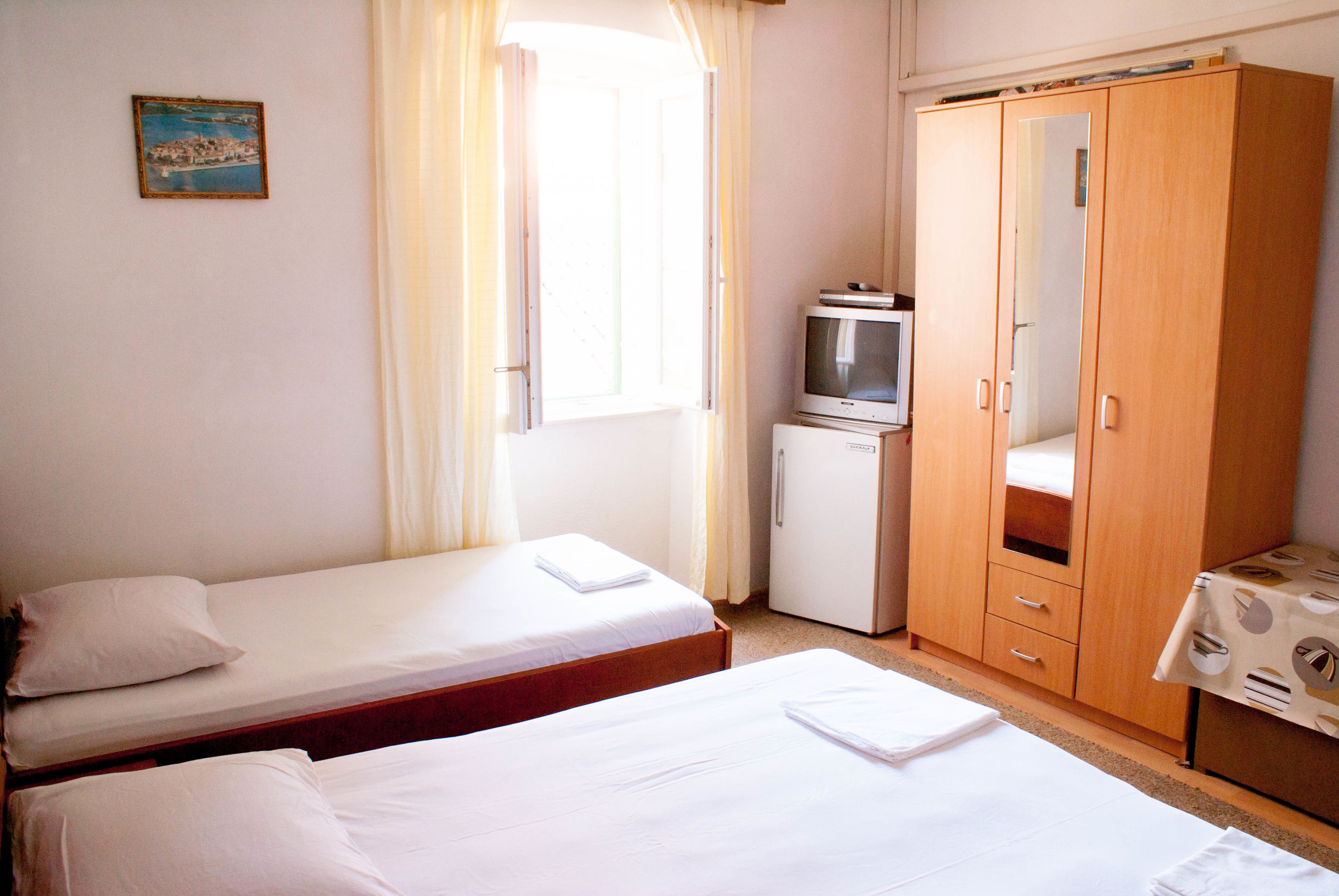 A room with two single beds, a small TV, a wardrobe, and a table with a tablecloth.