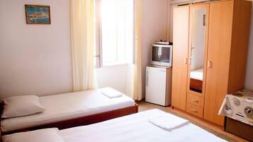 A room with two single beds, a small TV, a wardrobe, and a table with a tablecloth.