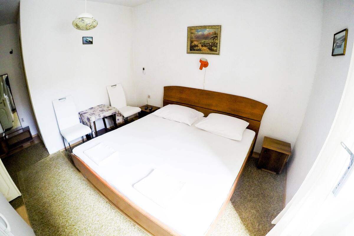 Quarto bem arrumado com uma cama grande, uma mesinha, uma cadeira e um quadro na parede.
