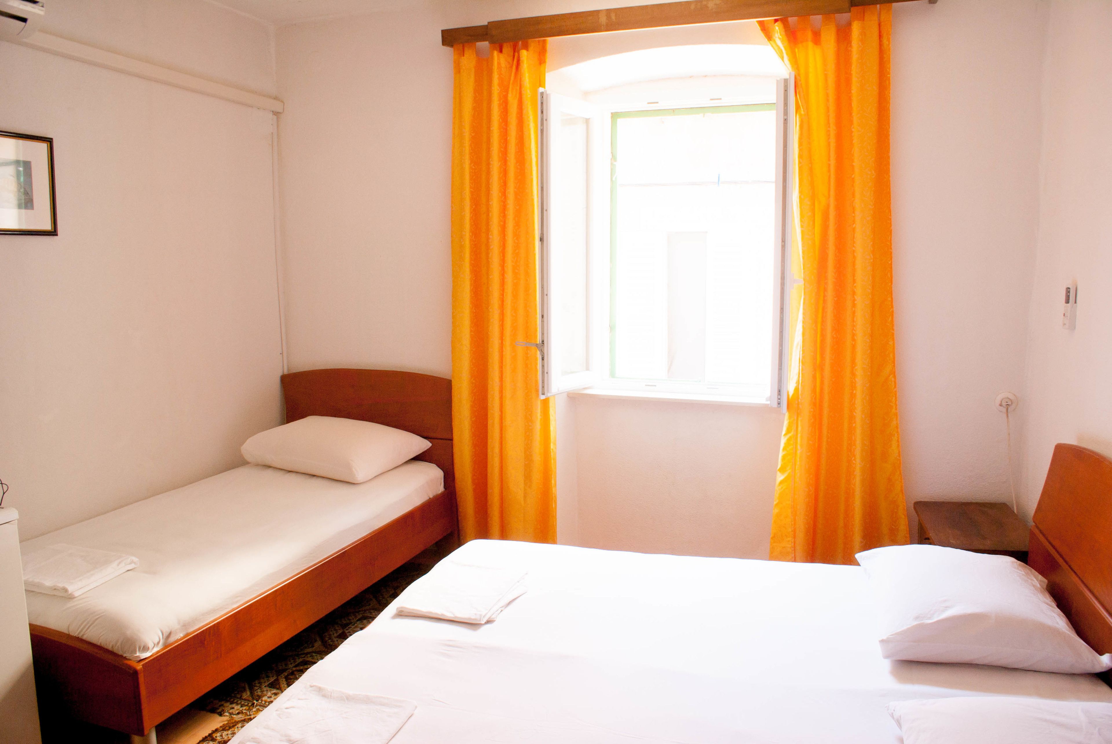 Een kamer met twee bedden, waarvan één groter en één kleiner, beide met witte lakens.