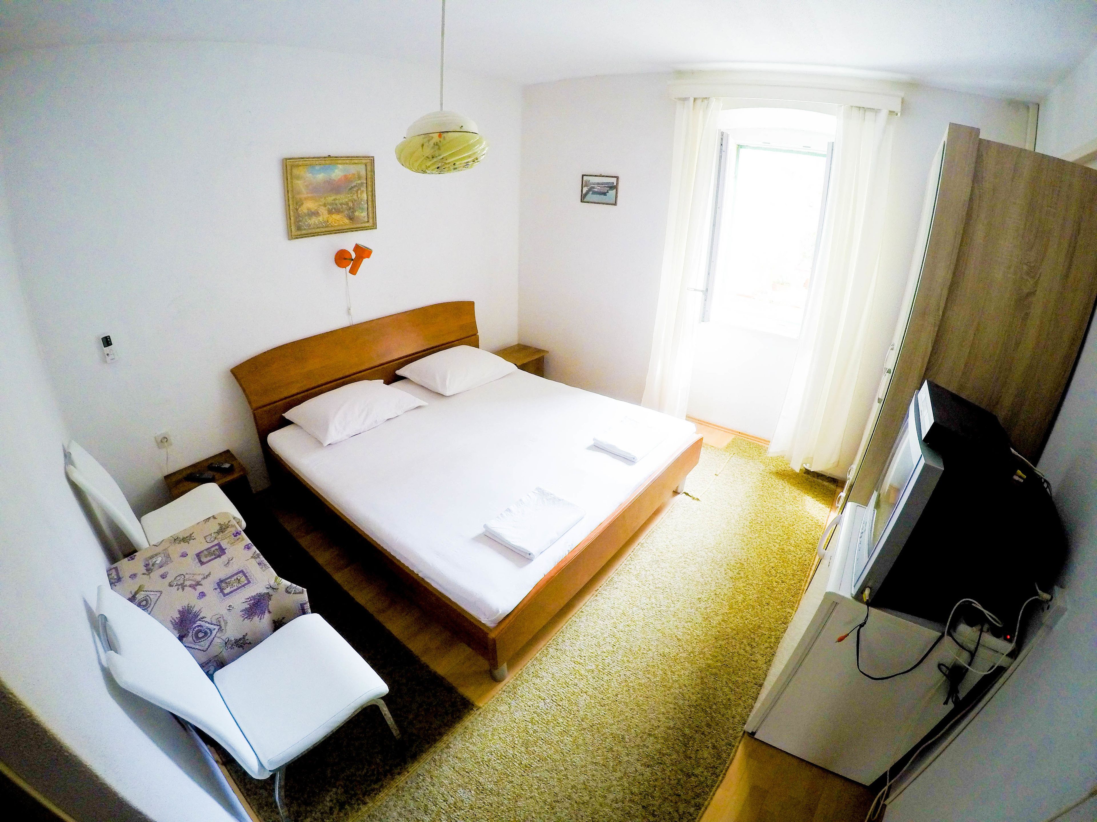 A neatly arranged hotel room with a single bed, a small bedside table, a chair, a television, and a window with curtains.