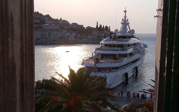 A large, multi-deck yacht docked at a marina with a backdrop of residential buildings and a clear sky.