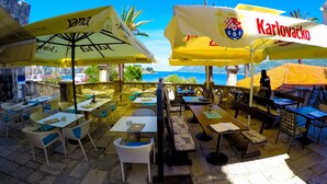 Café al aire libre con mesas y sillas bajo sombrillas amarillas, con vista a un paisaje pintoresco.