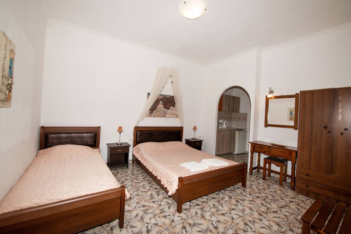 Un dormitorio con dos camas de madera, un escritorio de madera, un armario y un baño con lavabo y espejo.