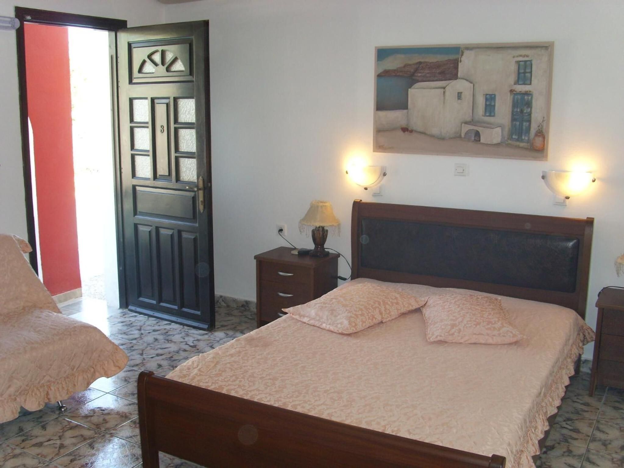 A bedroom with a bed, a nightstand, a lamp, a painting on the wall, and a door with a number.