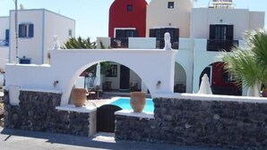 A coastal building with a stone wall, a pool, and a red door. - Sweet Heart Studio - Apartments (Santorini)