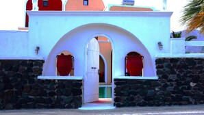 A building with a white facade, stone walls, and red doors. - Sweet Heart Studio - Apartments (Santorini)