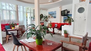 A spacious room with a large wooden table, red chairs, and a red sofa. There are several potted plants and a television mounted on the wall. - Sweet Heart Studio - Apartments (Santorini)