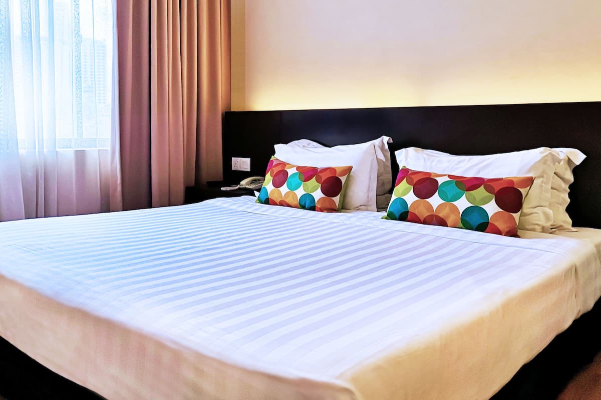 Habitación de hotel con una cama grande, dos almohadas de estampado colorido, una mesita de noche con un teléfono y una ventana con cortinas.