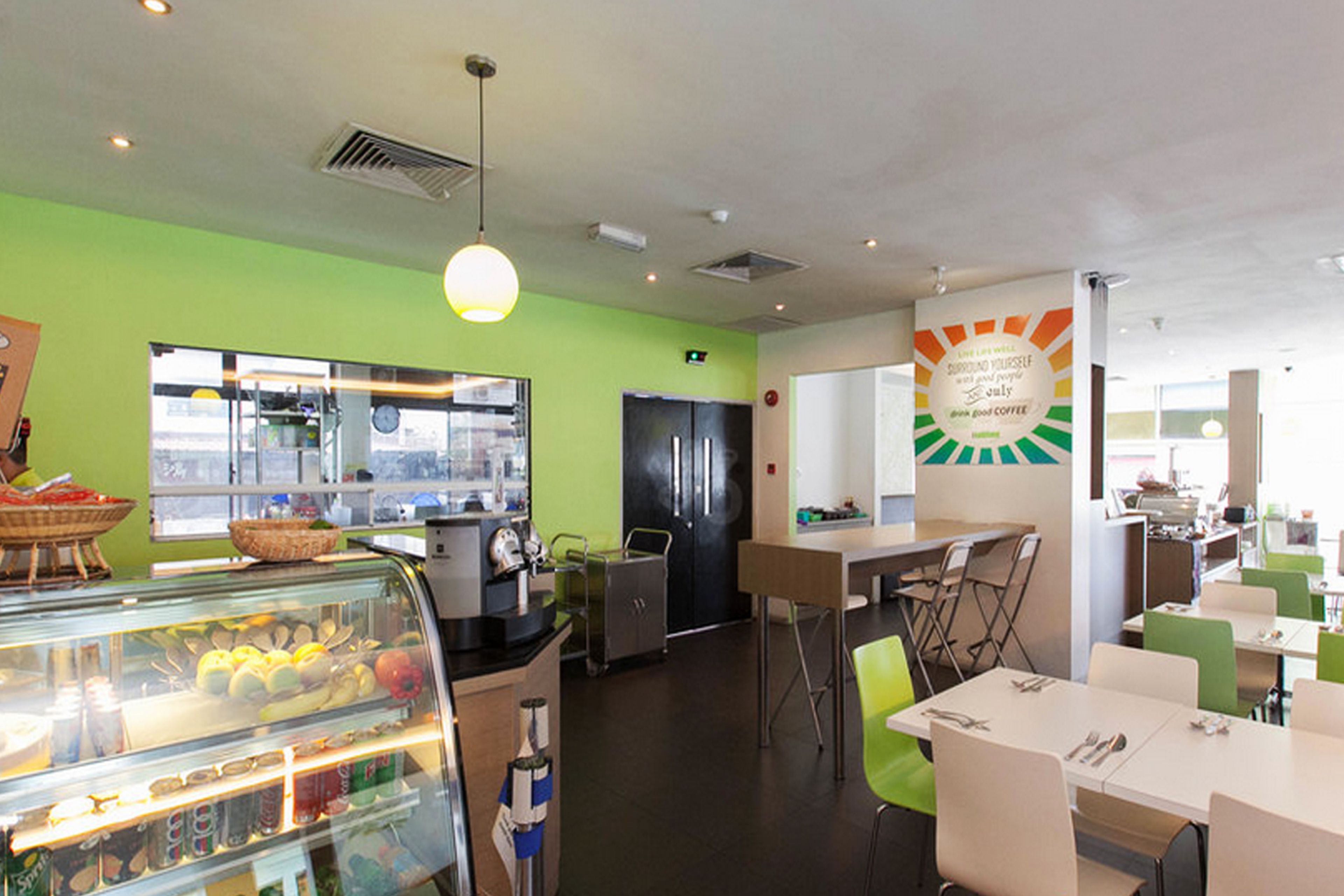 Una cafetería con un expositor de vidrio con comida, un refrigerador y zonas de estar.