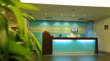 A reception desk with a blue backdrop, a television mounted above it, and a plant in the foreground.