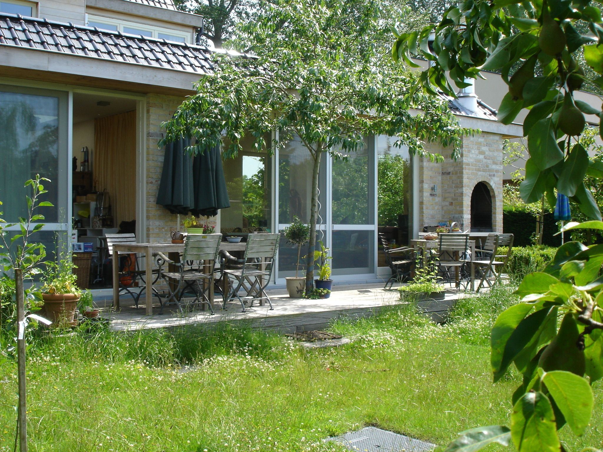 Eine Terrasse mit Sitzgelegenheiten, ein Steinhaus und ein Baum, der Schatten spendet.