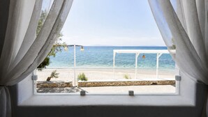 A window with white curtains, a view of a beach, and a white structure with hanging lights. - Blue Waves Suites & Apartments To Kyma (Paros)