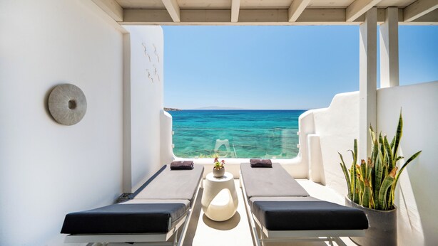 A balcony with two sun loungers, a small table with a flower vase, and a potted plant. - Blue Waves Suites & Apartments To Kyma (Paros)
