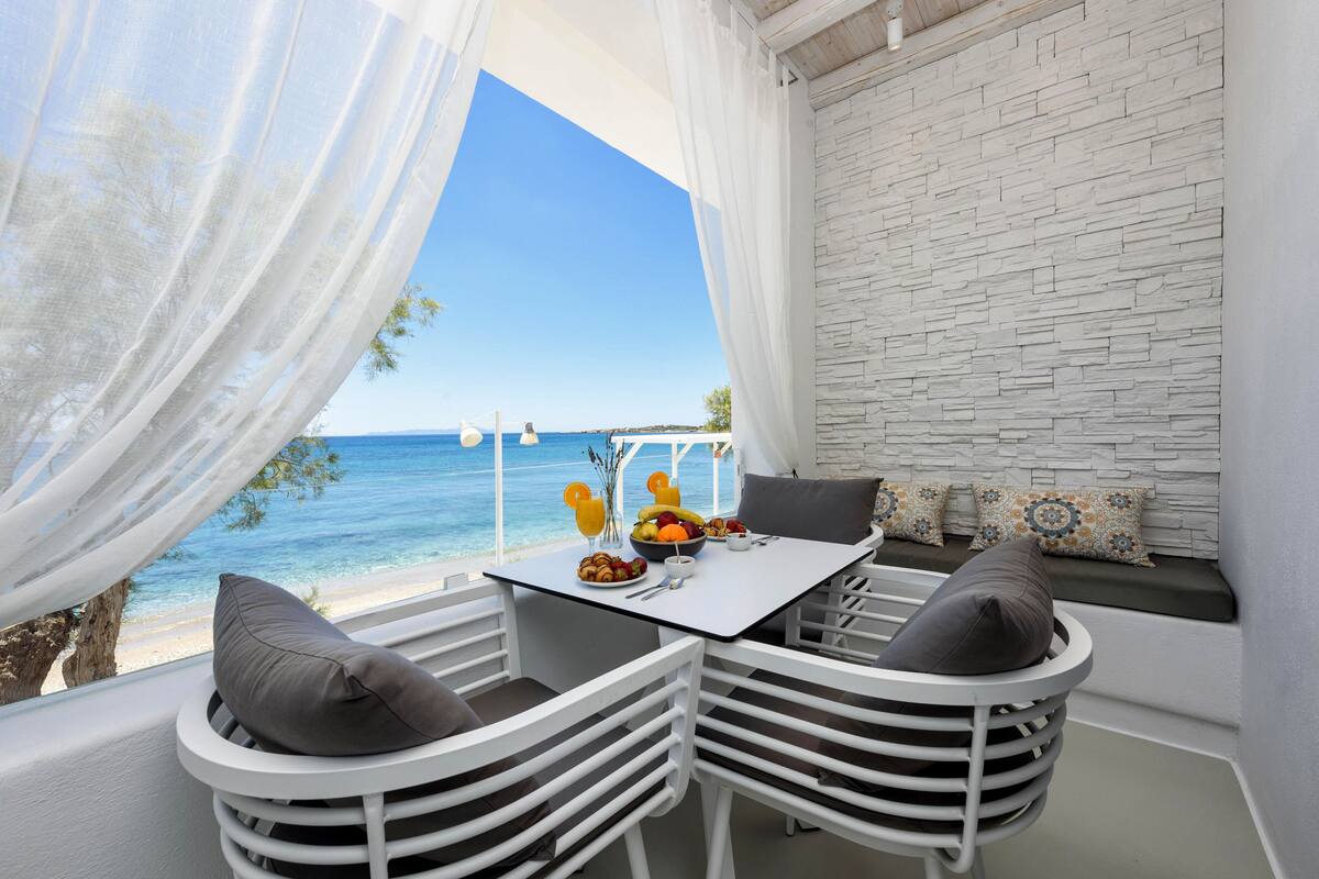 A balcony with a table and chairs, overlooking a beach.