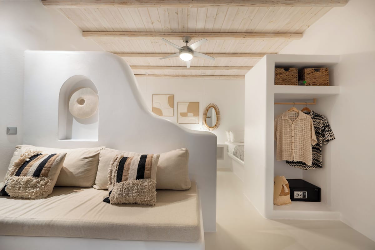 A modern bedroom with a curved headboard, a ceiling fan, a built-in wardrobe, and abstract wall art.