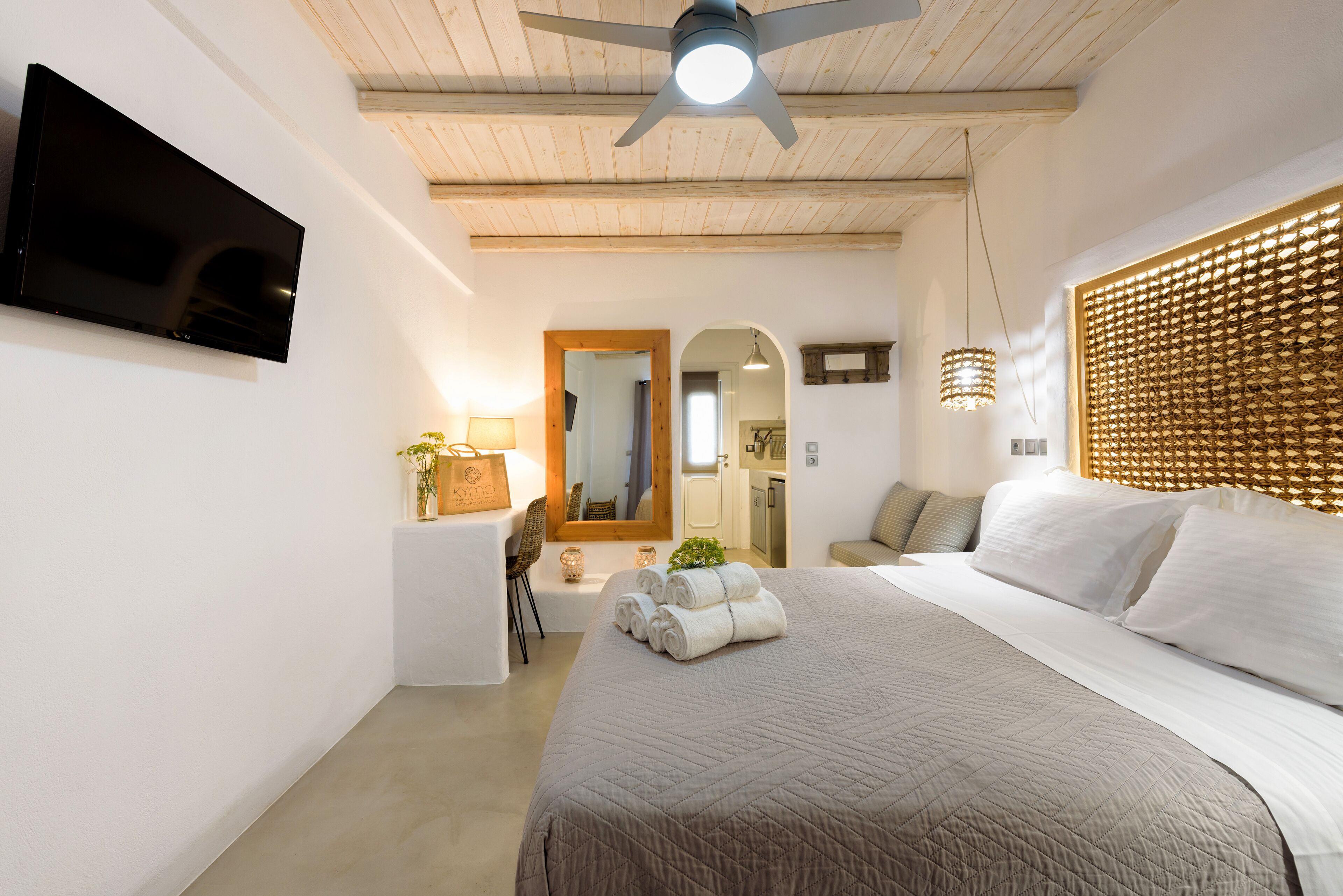 Camera d'albergo moderna con un letto grande, una TV a schermo piatto fissata al muro, una ventola a soffitto e un poggiatesta in legno.