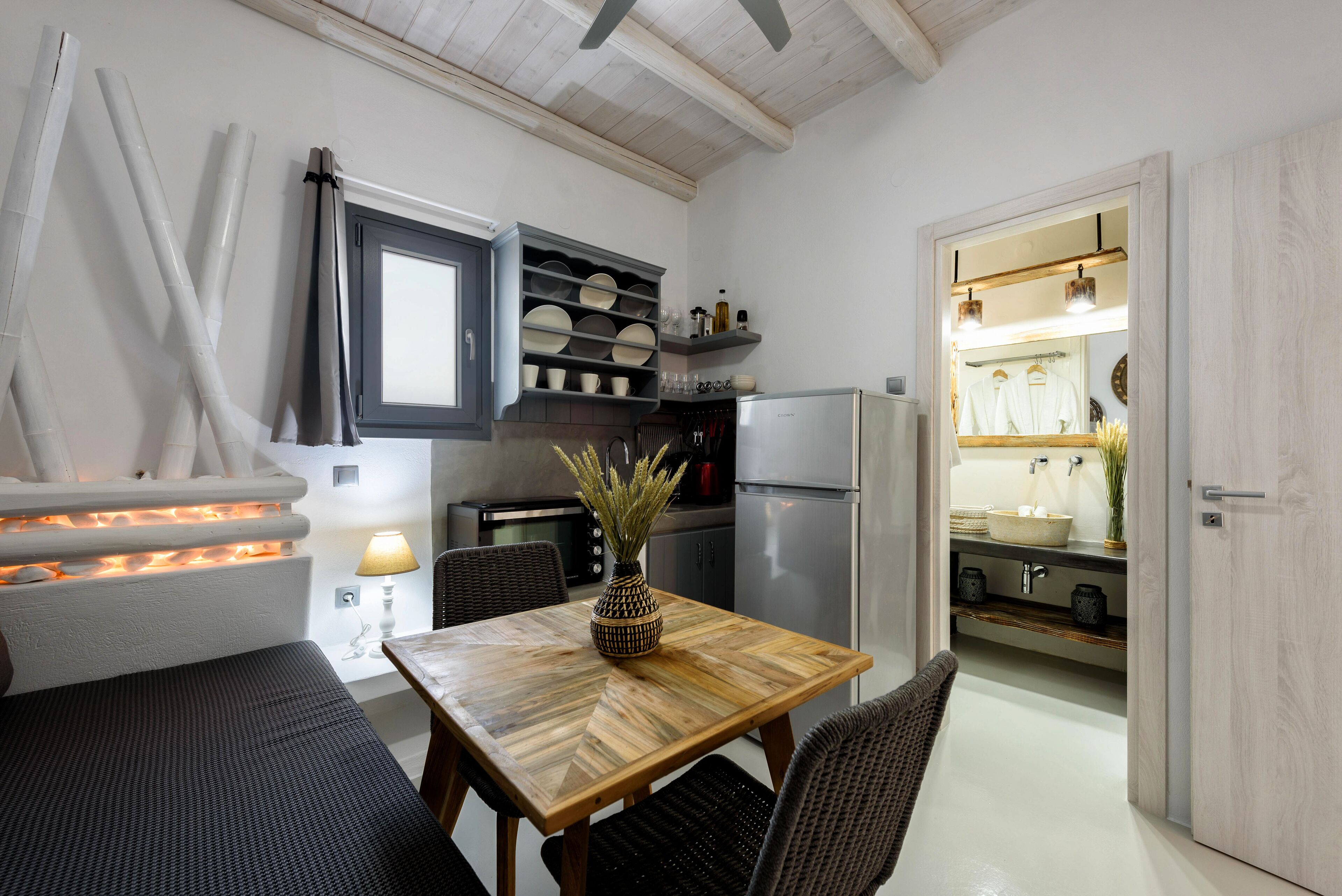 Cocina compacta con comedor, que incluye una mesa con sillas, un refrigerador y un estante empotrado con vajilla.