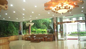 A spacious lobby with a modern chandelier, leather sofas, and a glass entrance leading to an outdoor area with greenery. - Fengyuyan Hotel (Guilin)