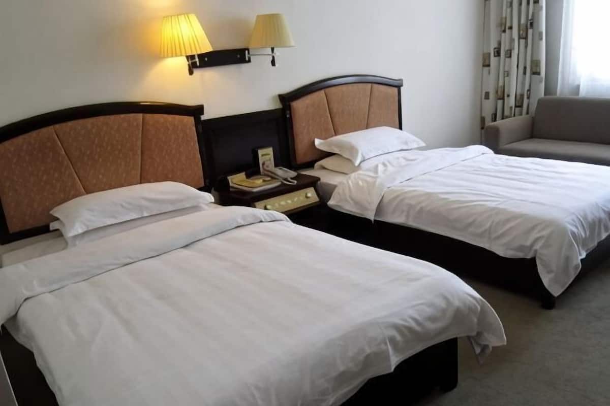 Two single beds with headboards, a bedside table with a lamp, and a chair in a hotel room.