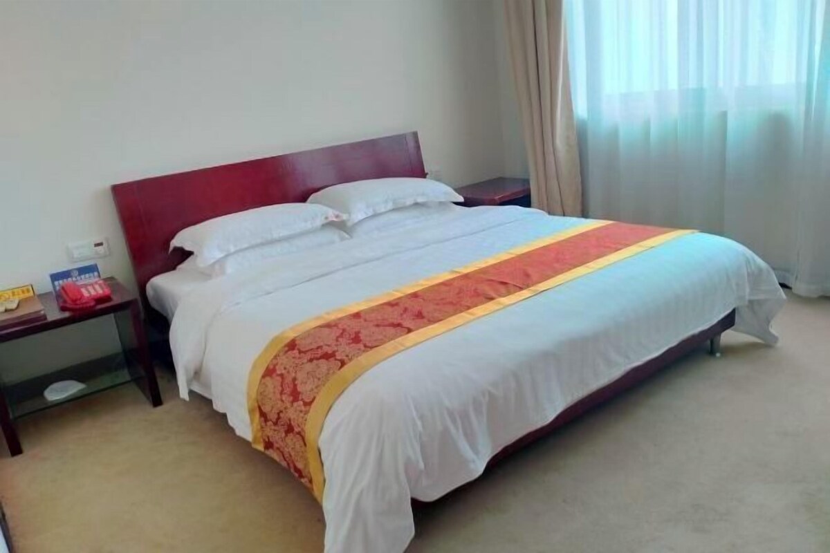 Une chambre d’hôtel avec un lit, une table de chevet, une commode et une fenêtre avec des rideaux.