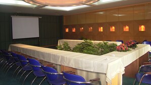 A conference room with a long table, blue chairs, a white screen, and a ceiling with skylights. - Fengyuyan Hotel (Guilin)