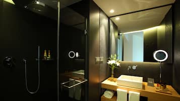 Un baño moderno con cabina de ducha de vidrio, tocador de madera con lavamanos y espejo con luz de aro.