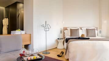 Una habitación de hotel moderna con cama, mesita de noche y una zona de estar con una bandeja de aperitivos y bebidas.