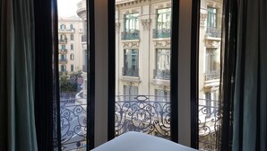 A hotel room with a large window offering a view of a cityscape with ornate balconies and buildings.