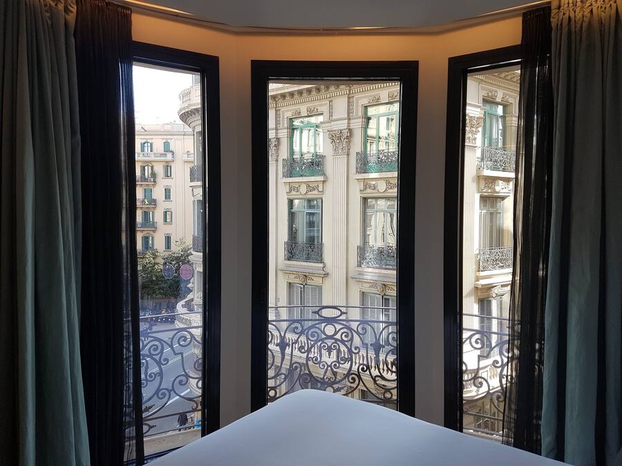 A hotel room with a large window offering a view of a cityscape with ornate balconies and buildings.
