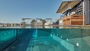 Una piscina cristalina de diseño moderno, rodeada por una terraza de hormigón y una estructura de madera con el logotipo de una estrella.
