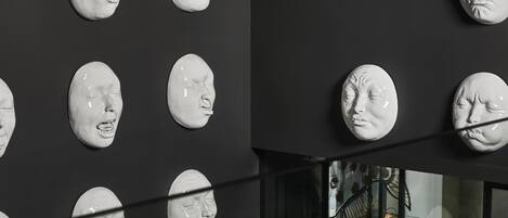 A wall with multiple white sculptures of faces.