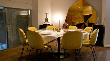 A dining area with a table set for six, surrounded by yellow chairs, a modern chandelier, and a large mirror reflecting the room.