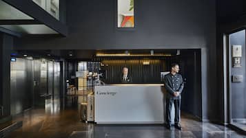 Eine moderne Hotelhalle mit einer Rezeption mit der Aufschrift "Concierge", Aufzügen und einem großen Fenster mit Blick zum Himmel.