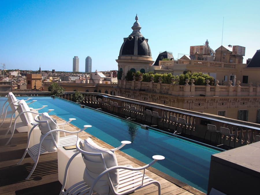 Piscina en la azotea con sillas blancas y vistas a edificios de la ciudad.