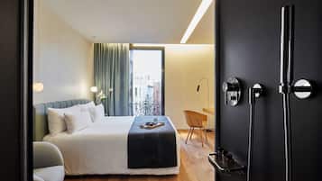 Habitación de hotel con cama, una silla, escritorio, ventana con cortinas y zona de ducha.