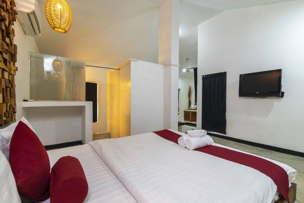 A hotel room with a large bed, a TV mounted on the wall, and a mirror above the bed.
