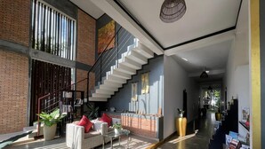 Un amplio salón con una escalera, una estantería y una zona de estar con cojines.