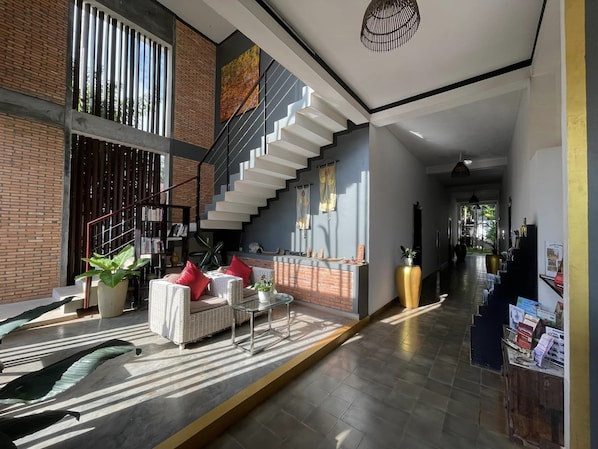 Un vaste espace de vie comprenant un escalier, une bibliothèque et un coin salon avec des coussins.